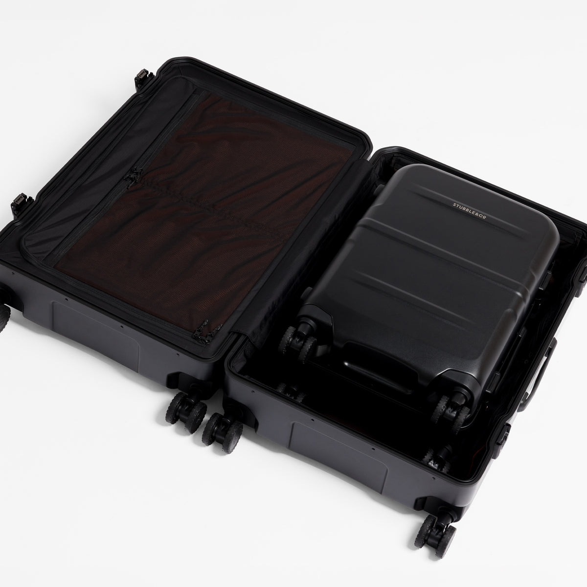 An open black hard-shell suitcase with wheels, showing a dark brown interior organizer panel and a matching black suitcase packed inside, photographed on a clean white background. [All variants]