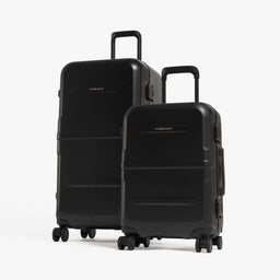 Two hard-shell spinner suitcases in black, one larger and one smaller, standing upright on a clean white studio background. [All variants]