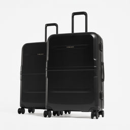 Two black hard-shell spinner suitcases standing upright on a light gray studio background. [All variants]