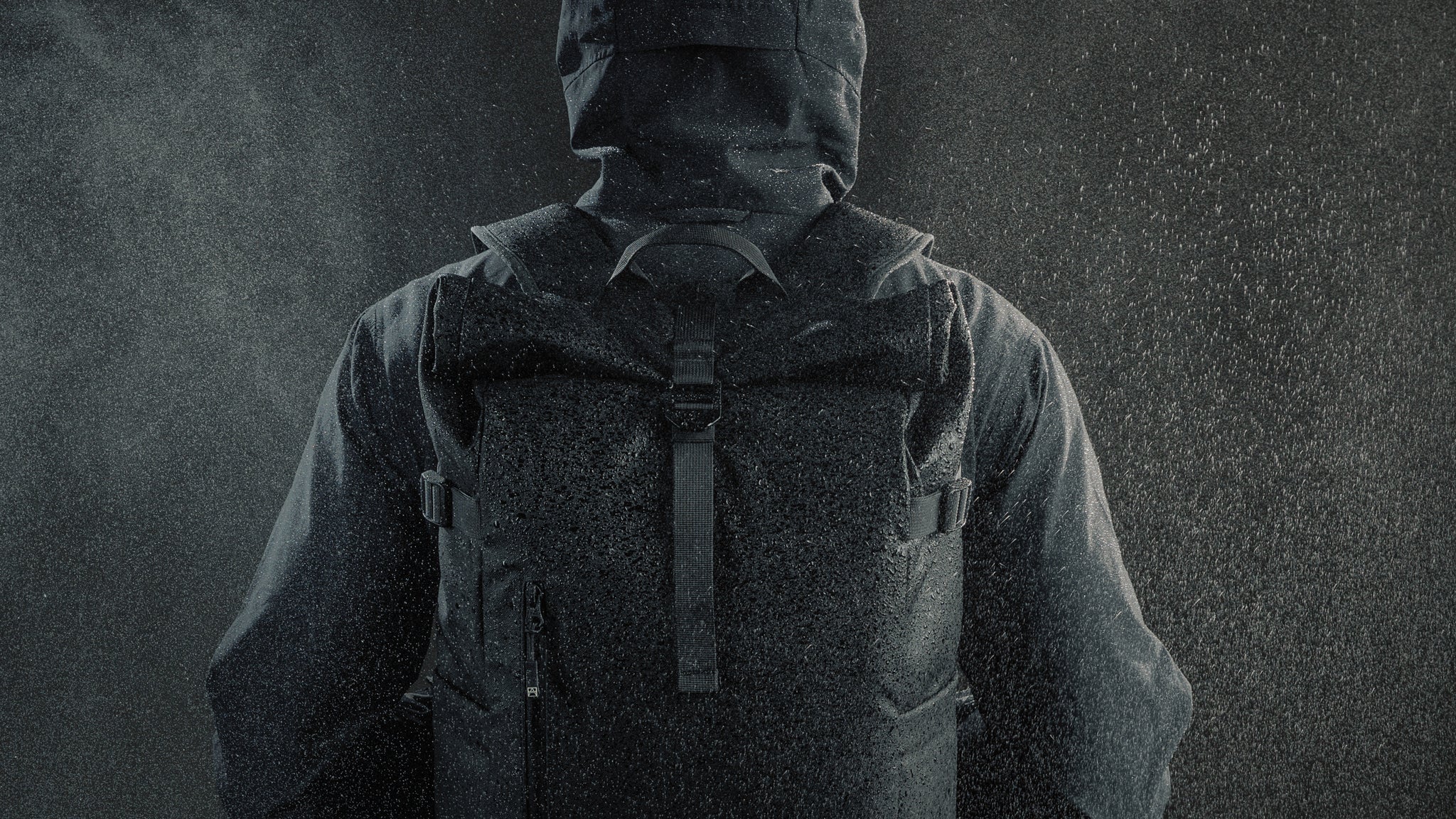Close up of back of a person wearing a black roll top backpack in the rain