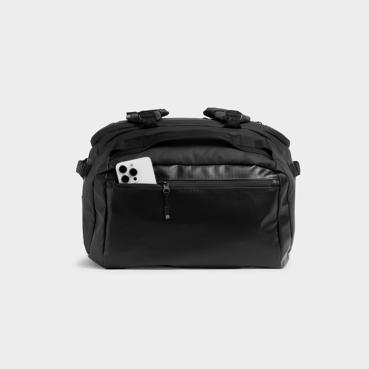 All Black duffel bag with a front zippered pocket containing a white smartphone, shown against a light gray studio background.