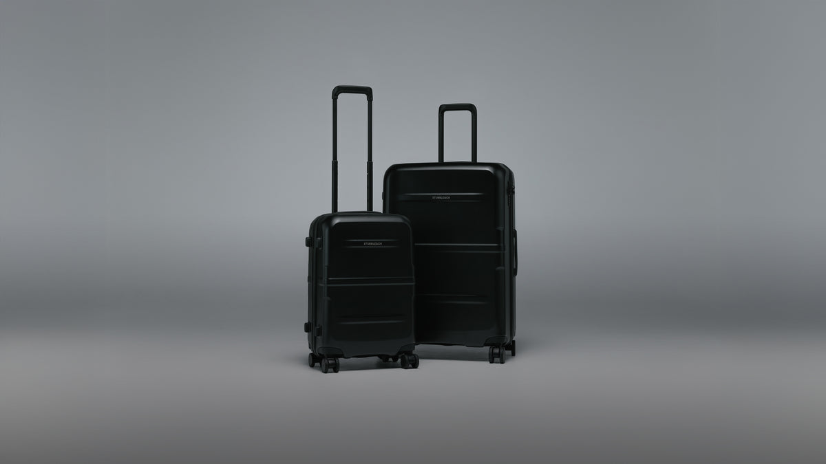Two hard-shell spinner suitcases in black, one smaller carry-on and one larger checked-size suitcase, standing upright on a smooth gray studio background.