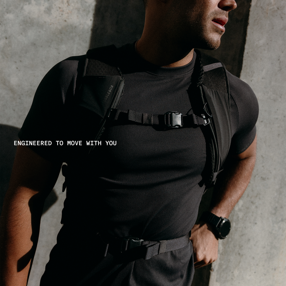 A man wearing the motion backpack 20l in charcoal on his back with the chest and waist straps done up with the range slogan annotated- 'engineered to move with you"