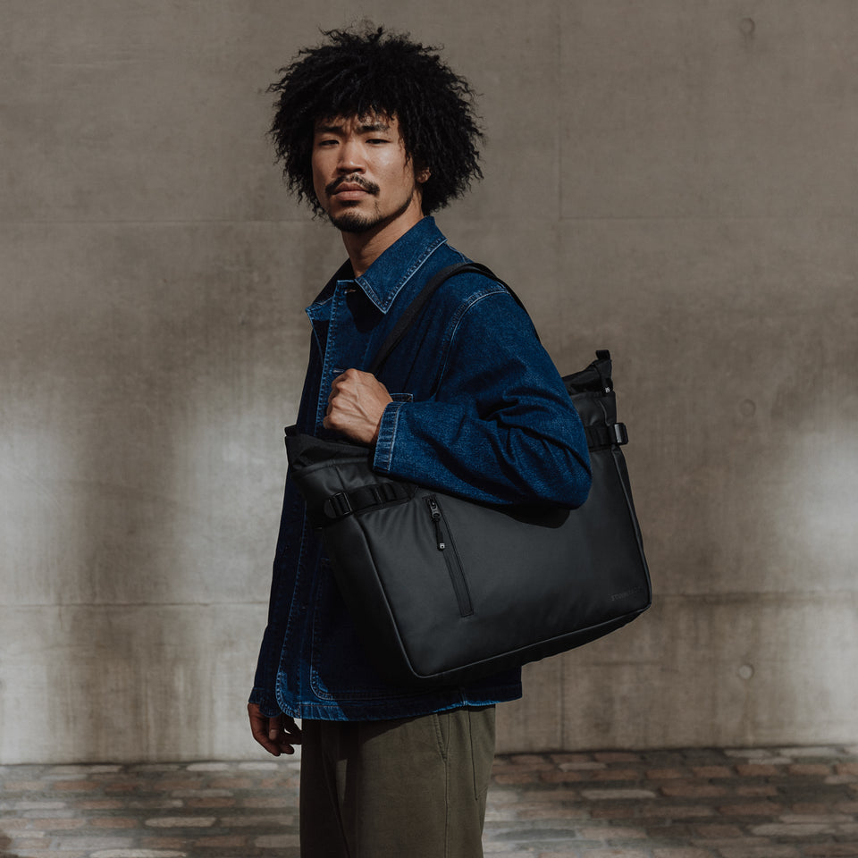 Man with a black tote bag standing by a wall