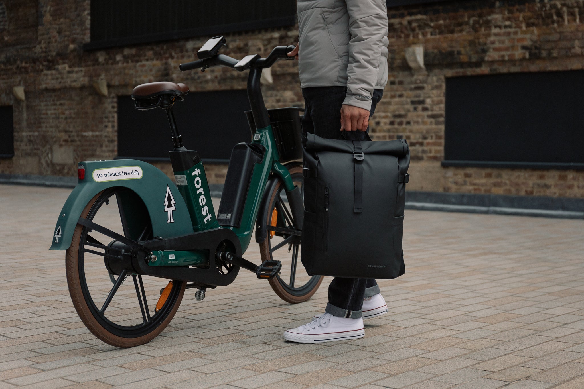 A man standing next to an e-bike holding a black backpack by his side