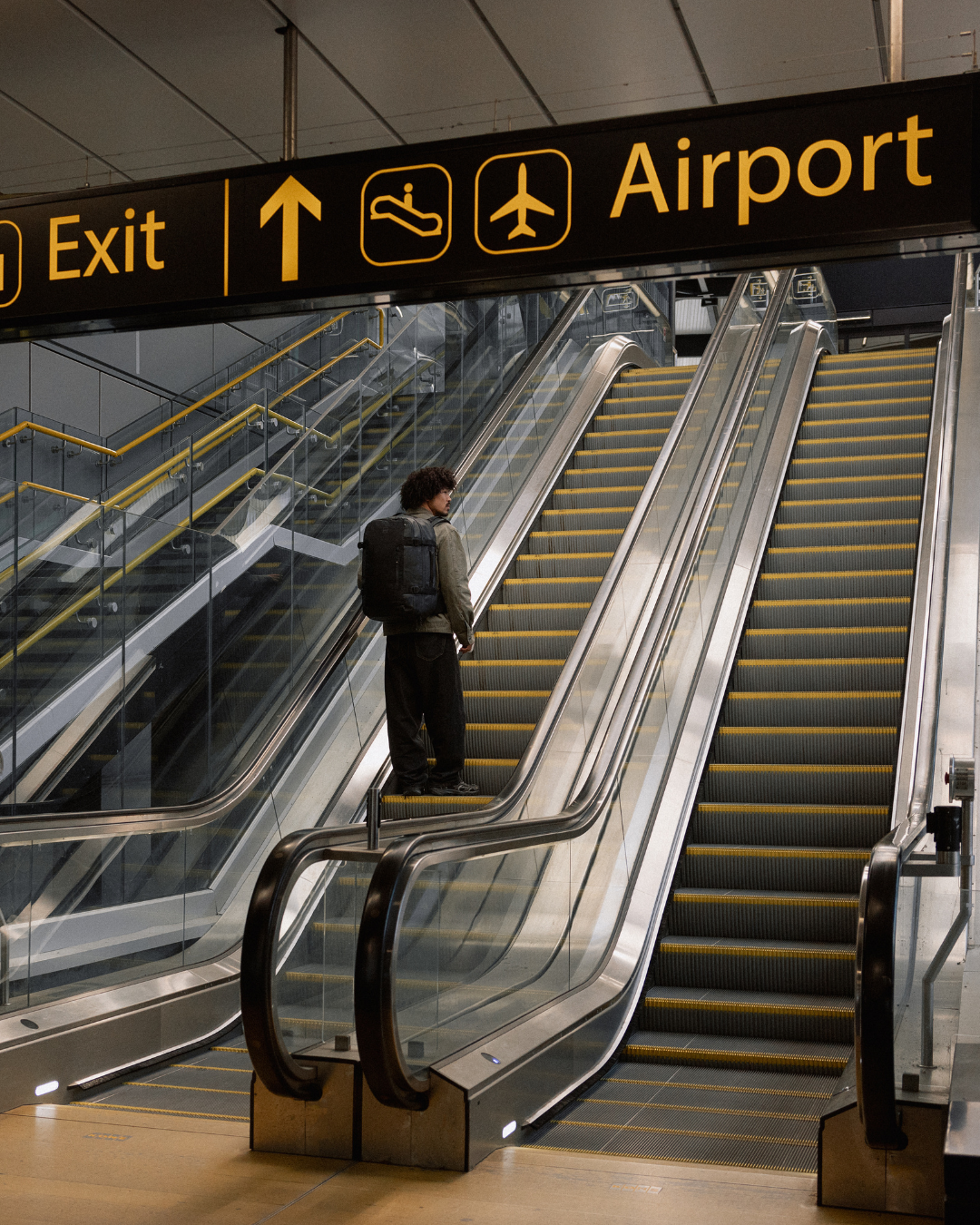 Man wearing travel backpack travelling up escalator in airport