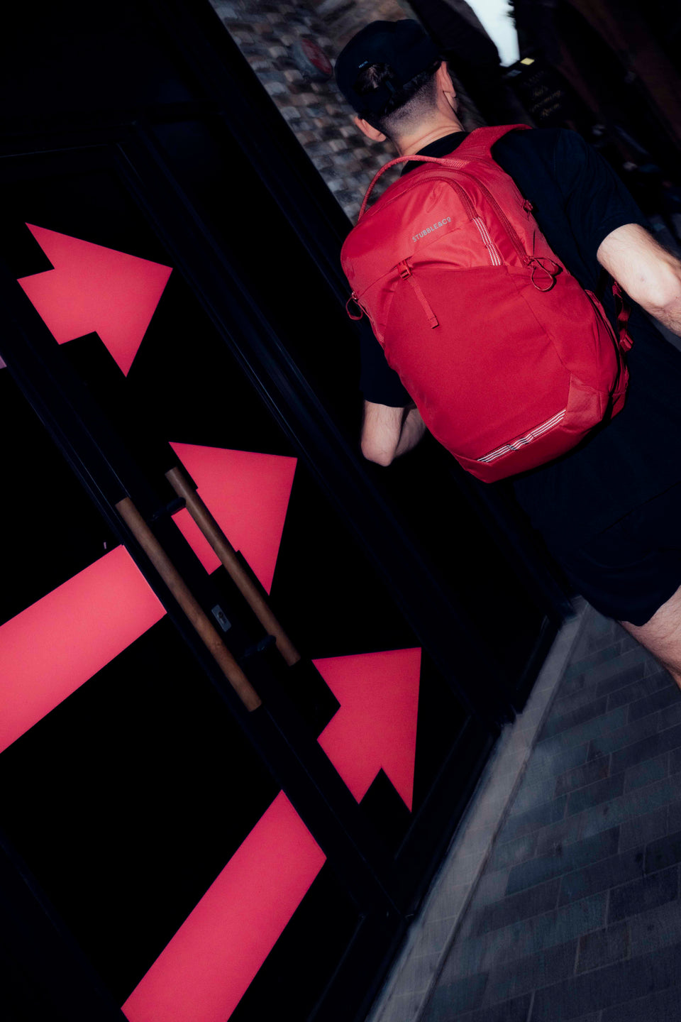 A man running along the street with a magma motion backpack 20l on his back as he follows red arrow on the wall to showcase the route