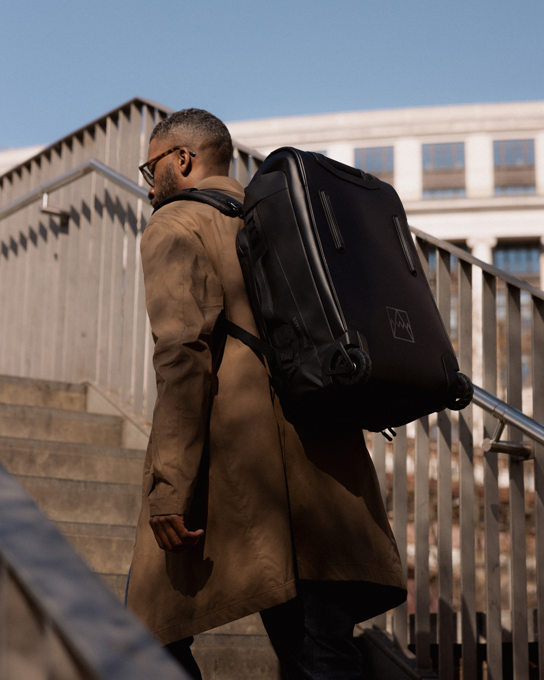 Man walking upstairs carrying wheeled backpack on his back