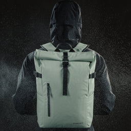 Person wearing a rain coat and the Roll Top Backpack in Matcha green with water spray