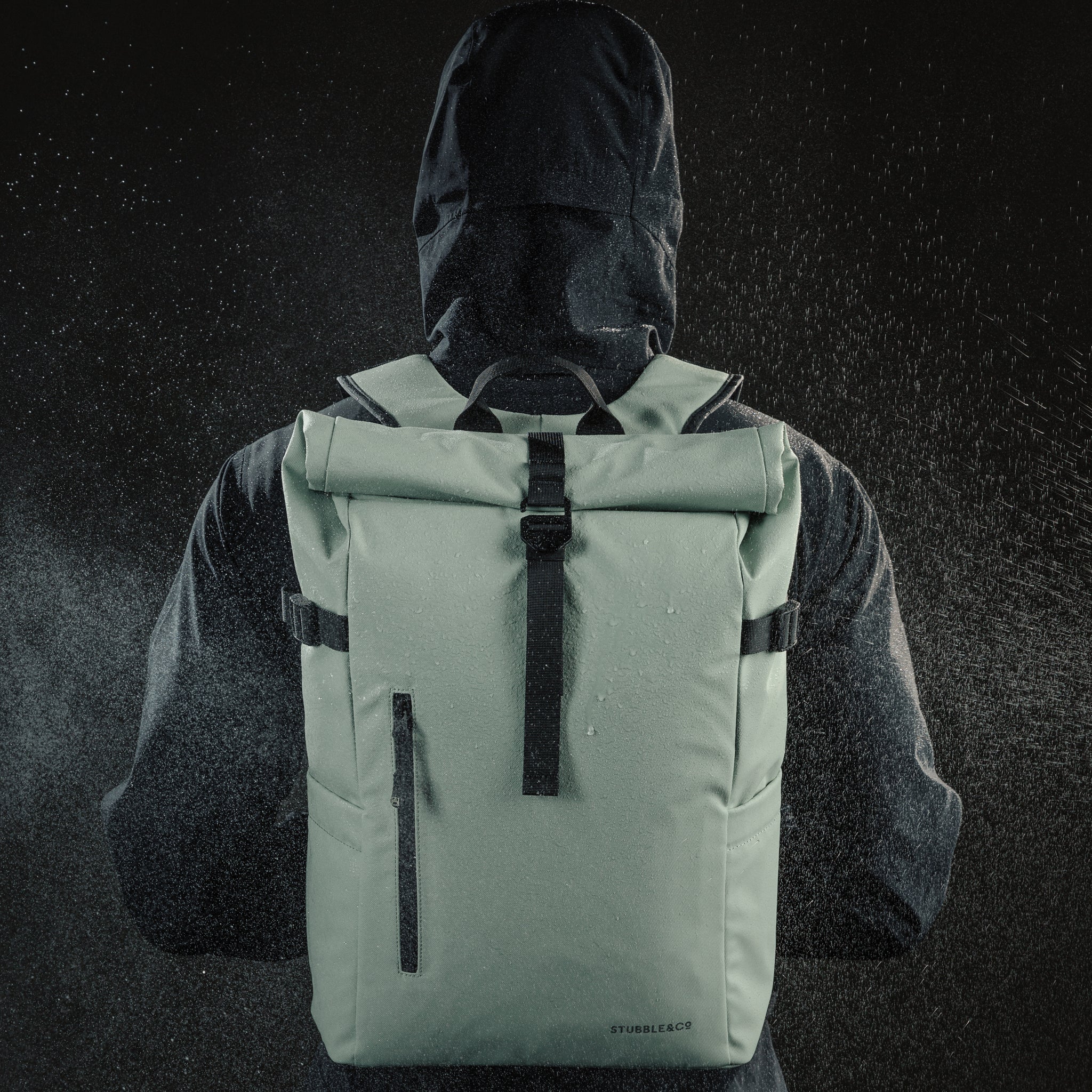 Person wearing a rain coat and the Roll Top Backpack in Matcha green with water spray