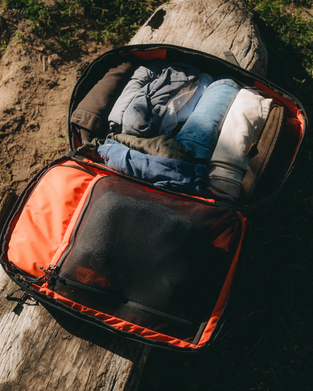 Open Travel Backpack on log filled with travel clothes and supplies