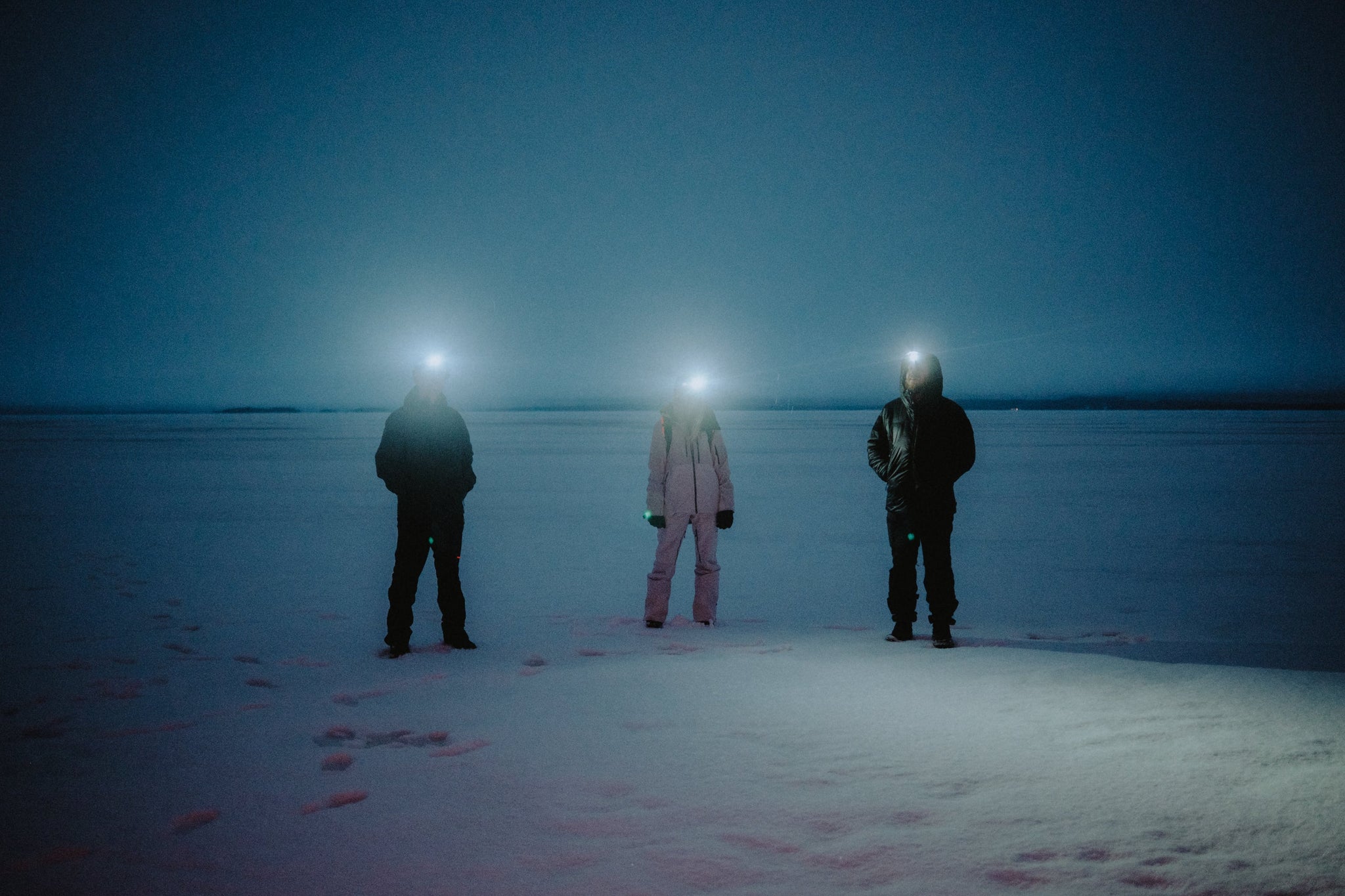 Three people standing at night in the snow with head torches