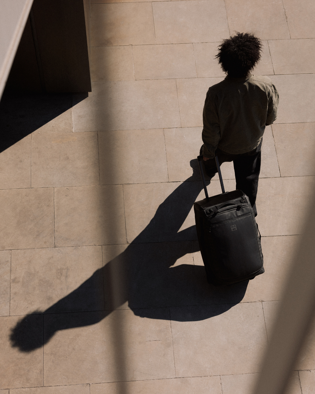 Overhead shot of man walking outside in the sun wheeling a suitcase behind him