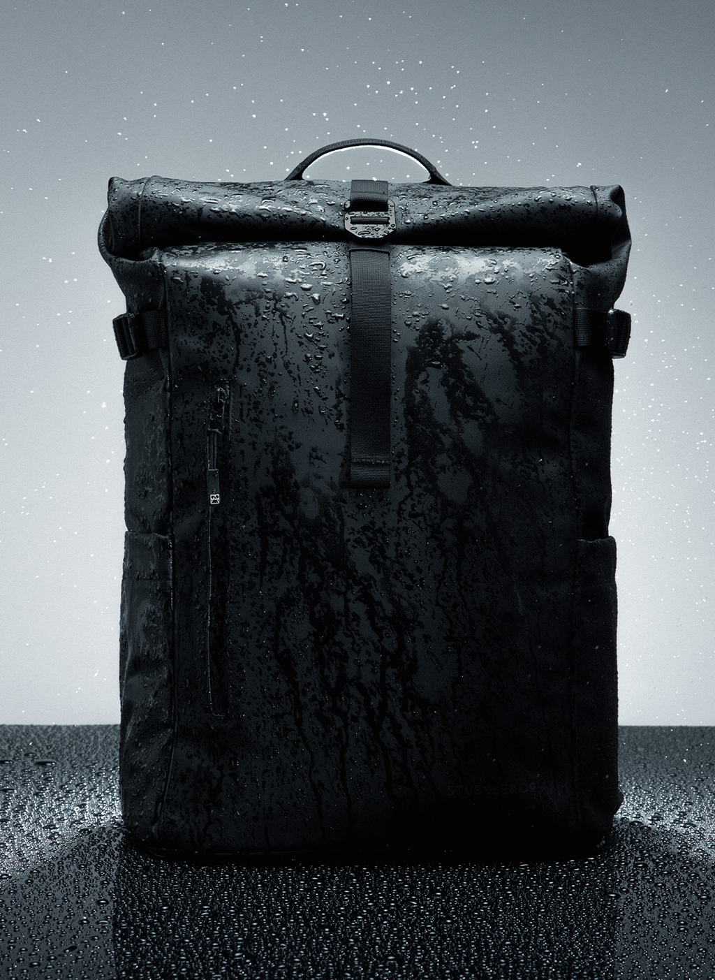 Black Roll Top backpack on a gray background with water beads on the fabric 