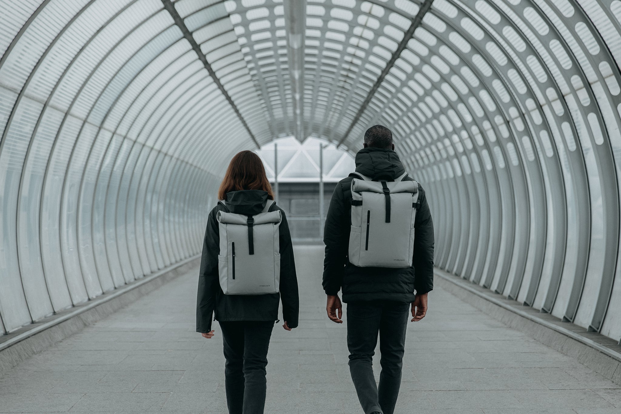 Man and women walking down tunnel and wearing grey backpacks