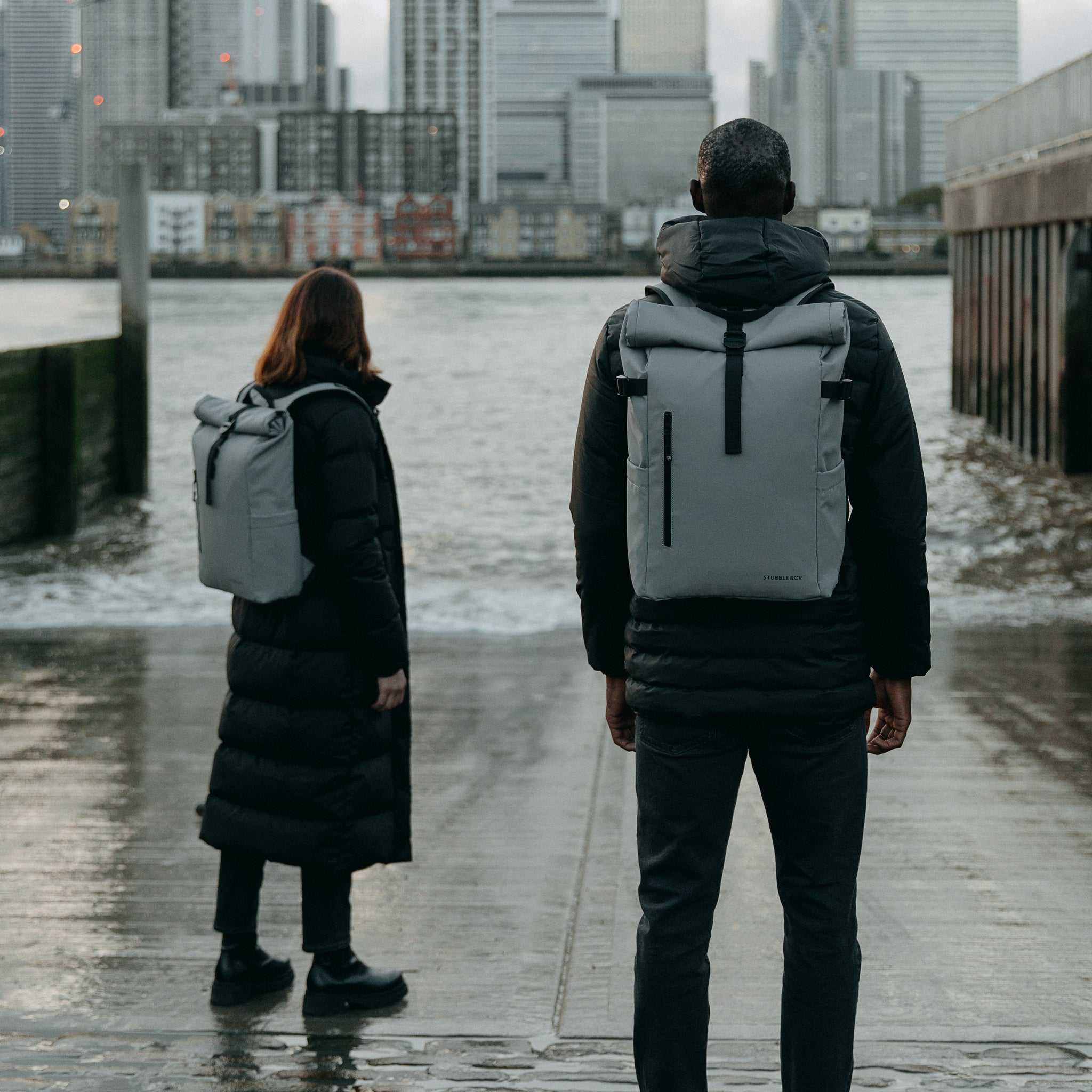 Man and women wearing Concrete grey Roll Top backpacks in a city