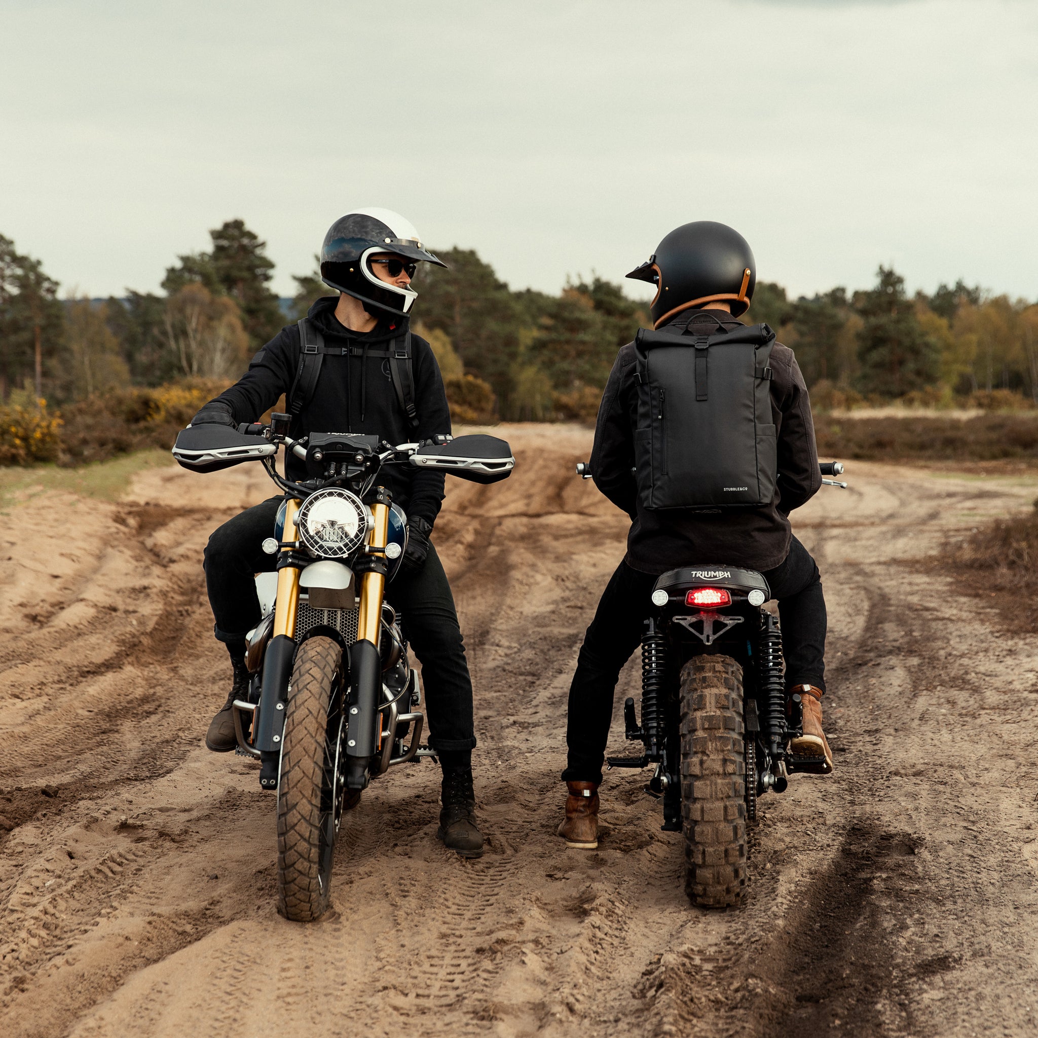 Two men on motorbikes wearing The Roll Top backpack in All Black