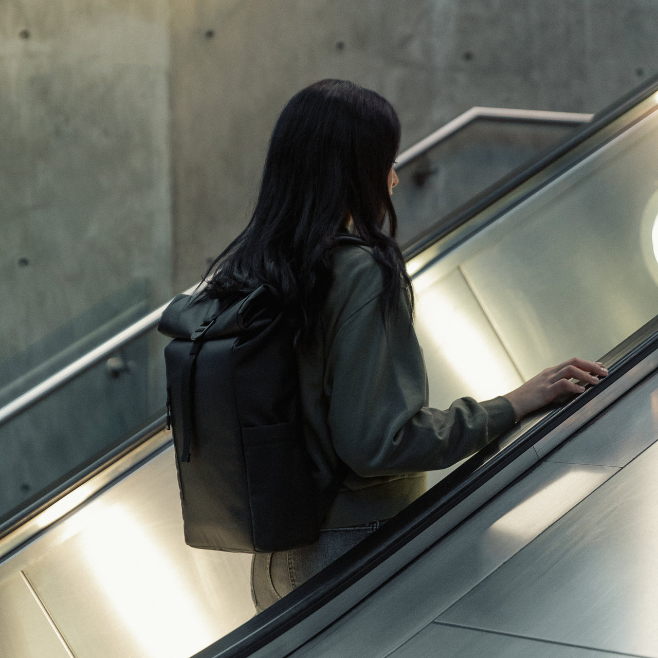 Women wearing an All Black Roll Top Mini backpack going up an escalator