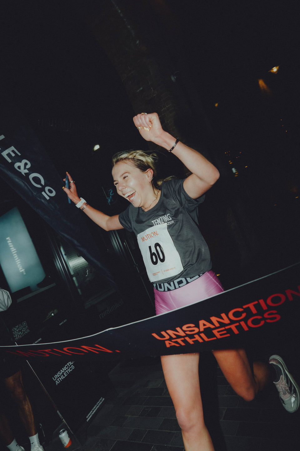 A woman crossing the line of a running race for the Stubble&Co and Unsanctioned Athletics event as she goes through the finisher banner