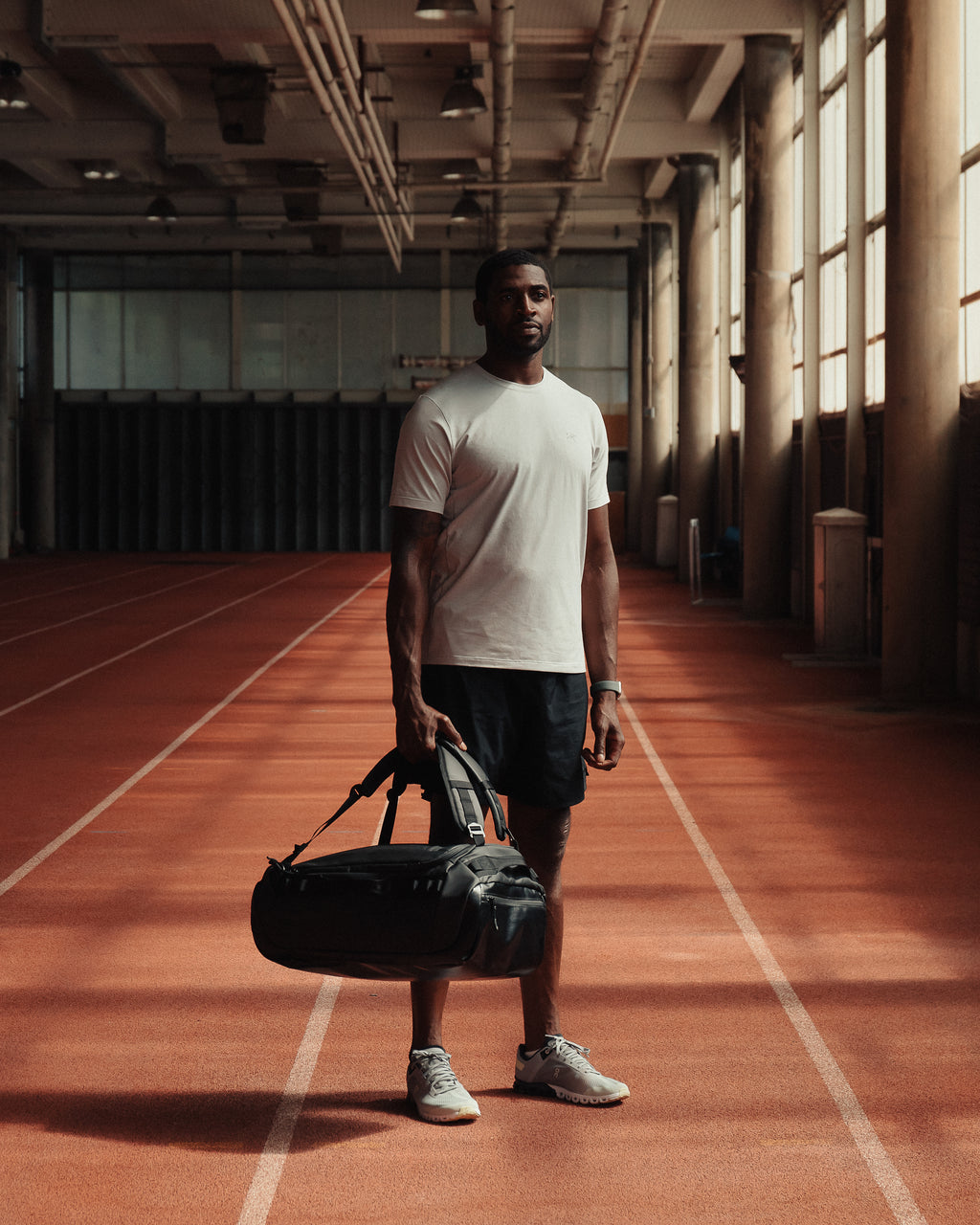 Man standing on an indoor running track and holding a black holdall kit bag