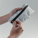 Close up of hands holding the Off White packable Ultra Light Crossbody Bag packed into it's pocket