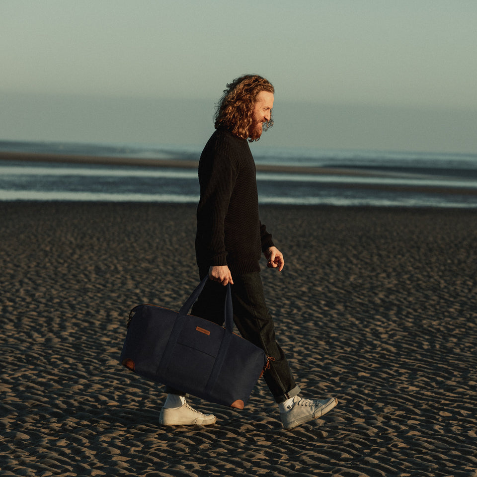 Man carries Weekender XL Duffle Bag on a beach