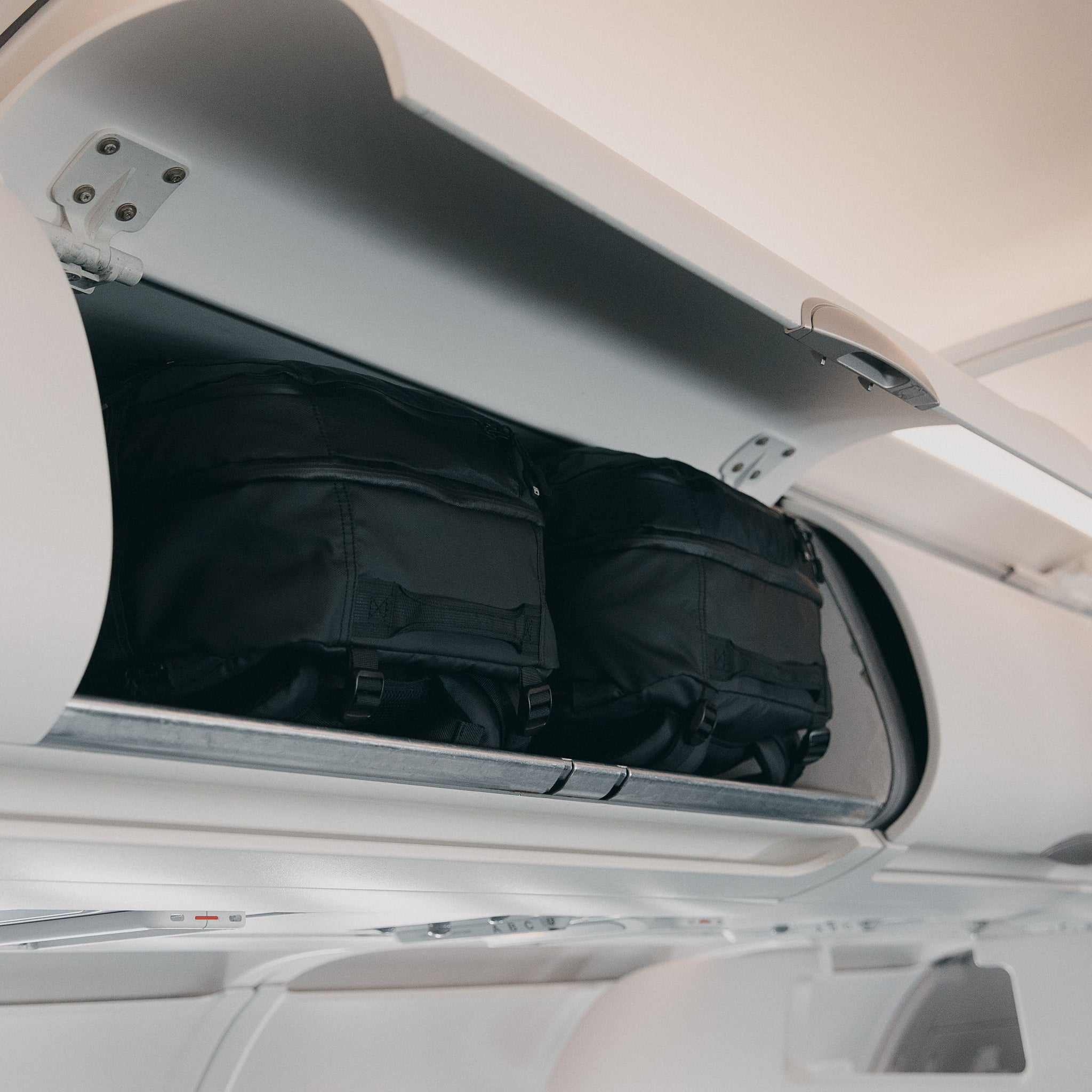two All Black Adventure bags in the overhead lockers on an airplane