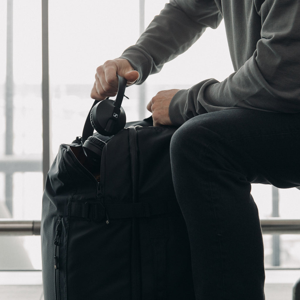 A man putting his head phones into the top pocket on an All Black Adventure Bag