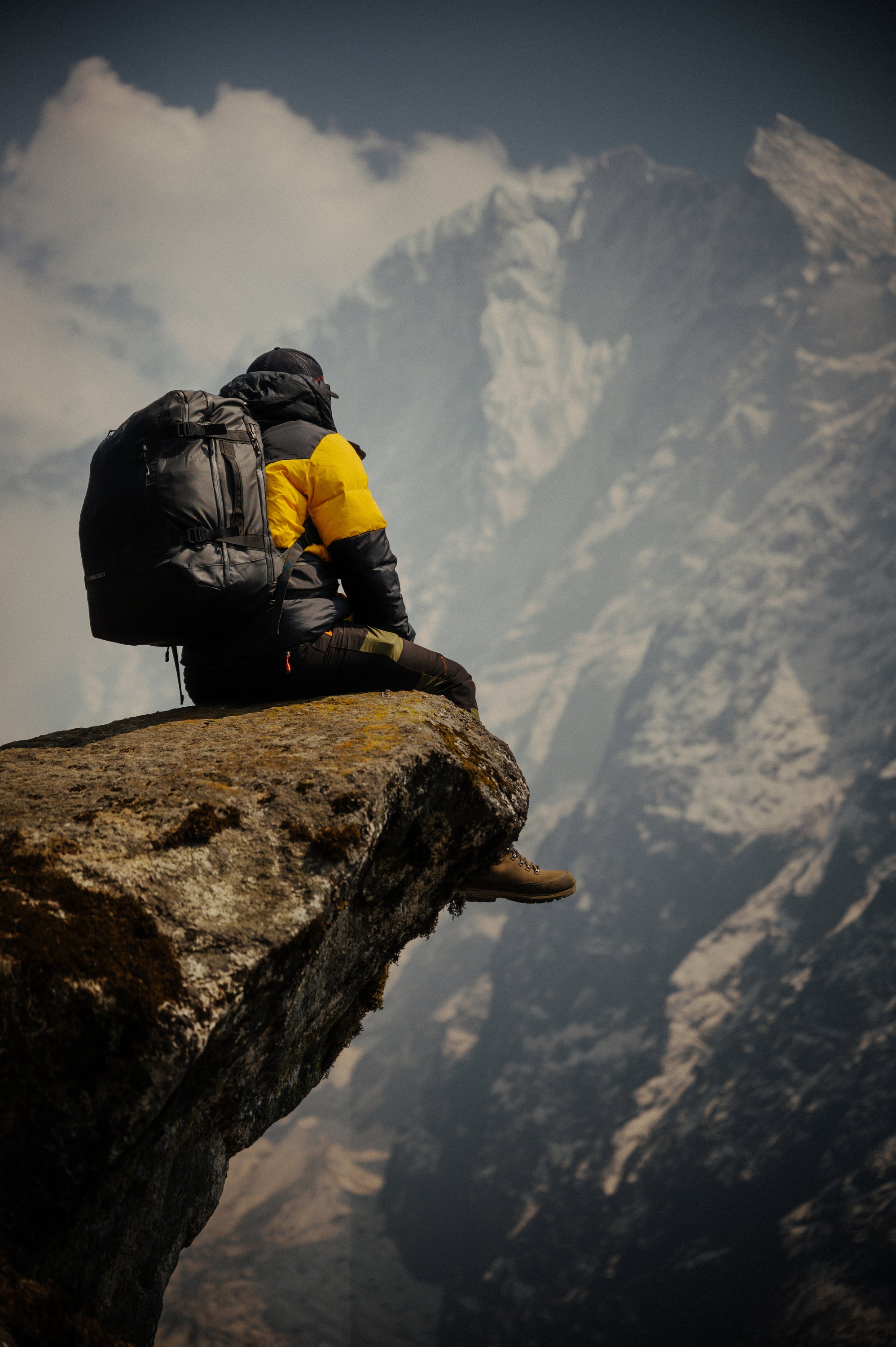 Man sitting on the edge of a cliff wearing a black Adventure Bag