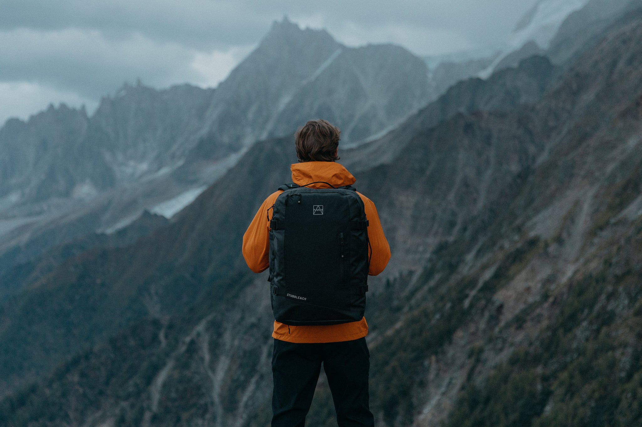 Man with black backpack looking over mountains
