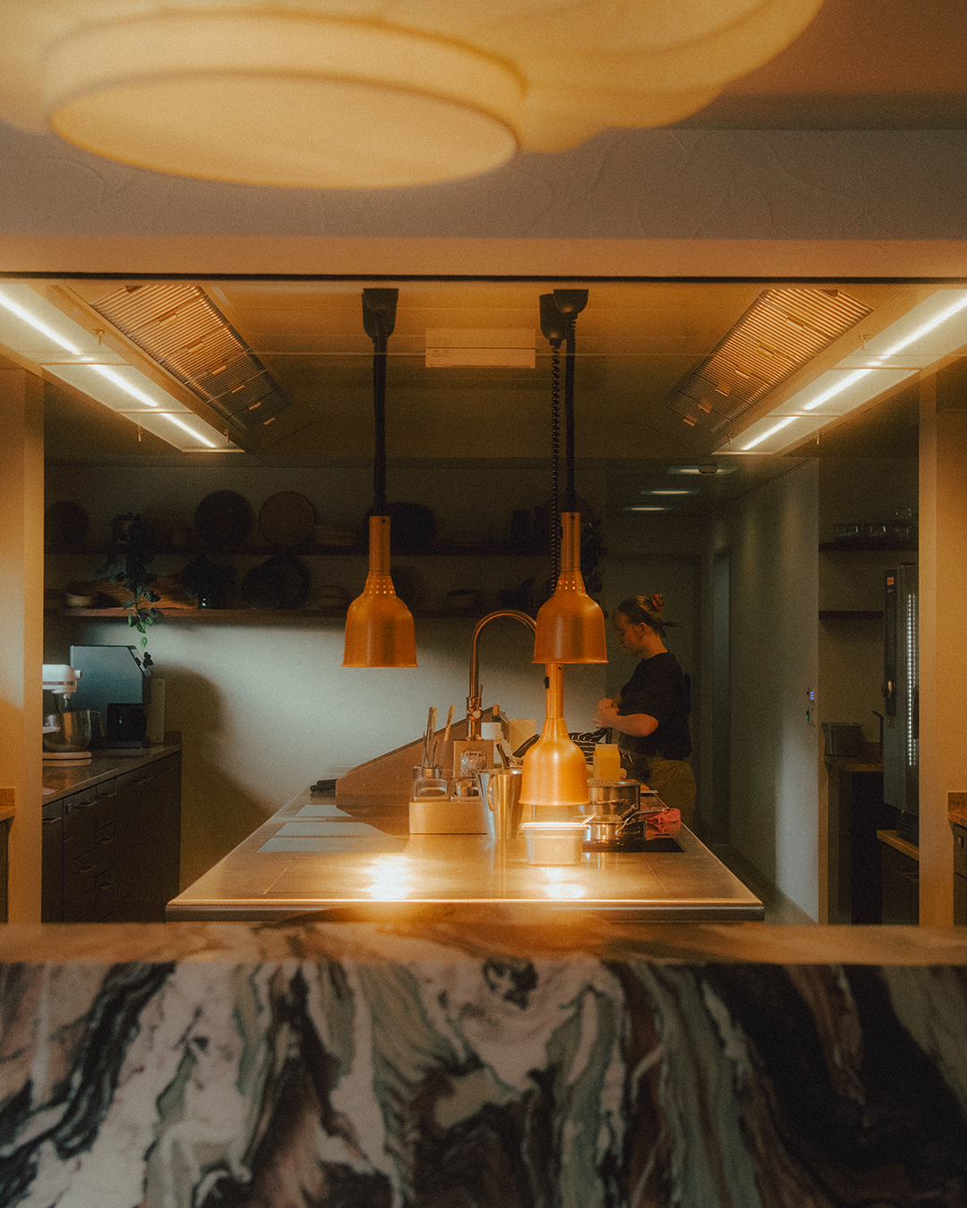 Restaurant kitchen with pendant lights and a person working.