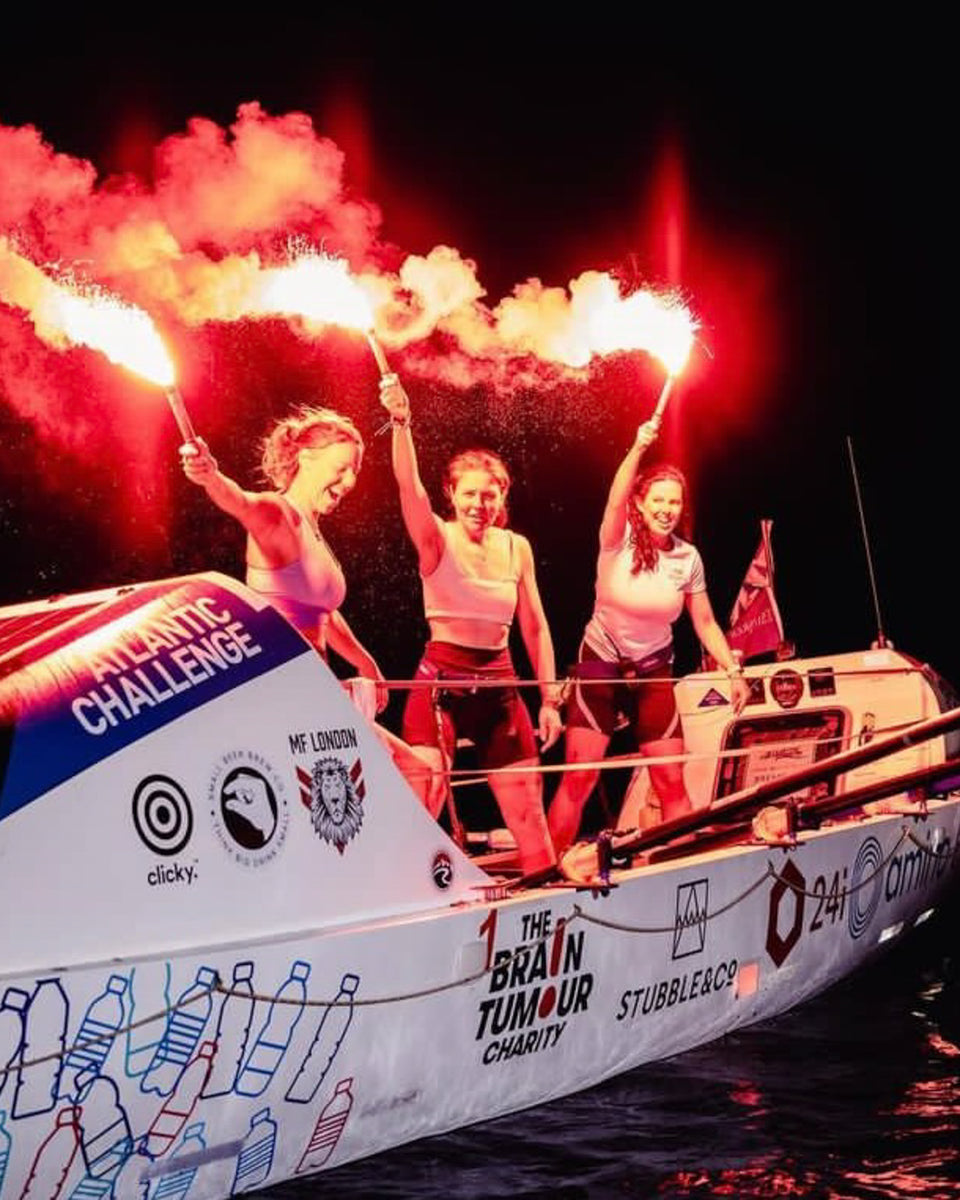 Women celebrating with red flares at night on a rowing boat