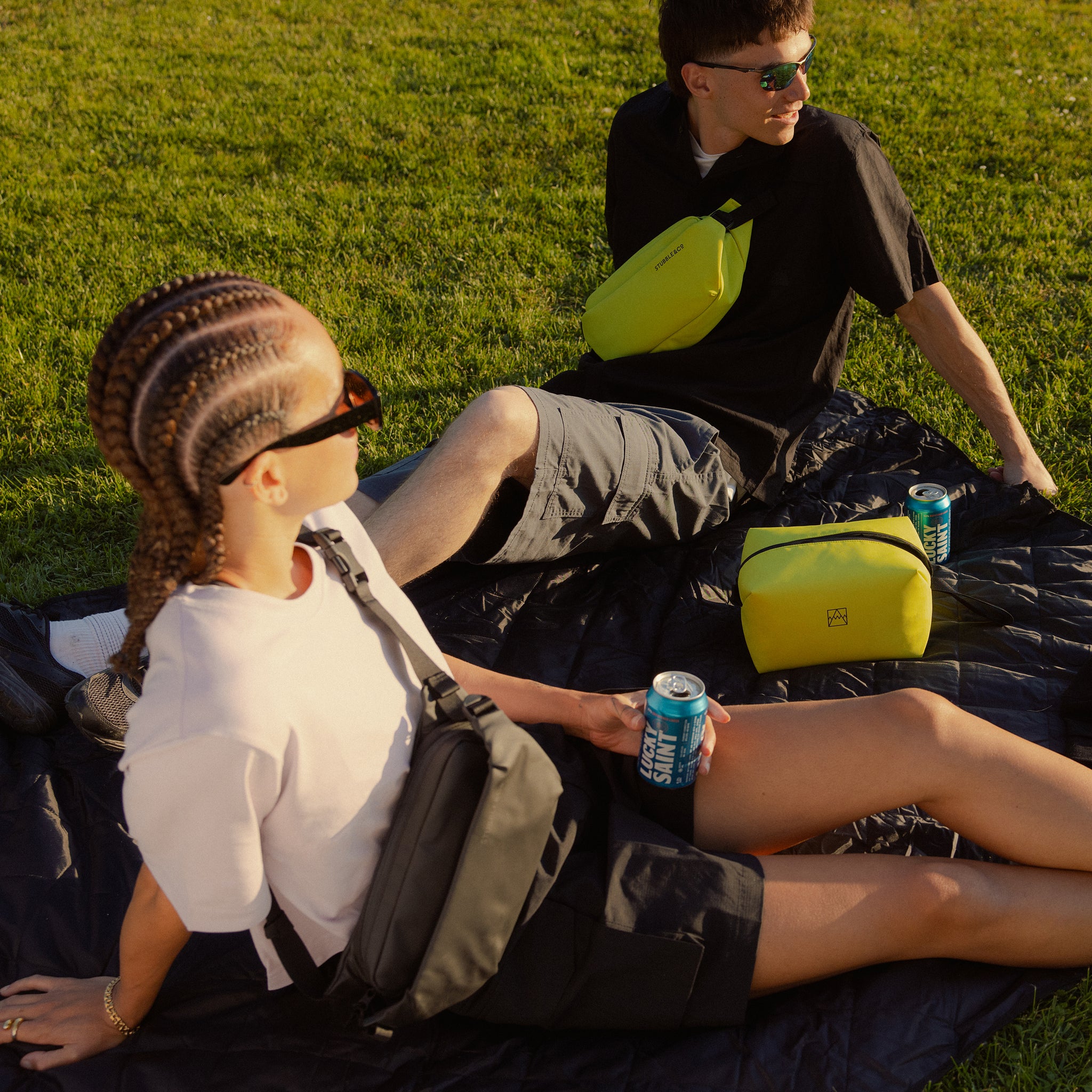 A man and woman sitting on a picnic blanket in a field with lucky saint beer from their Volt Beer Bag