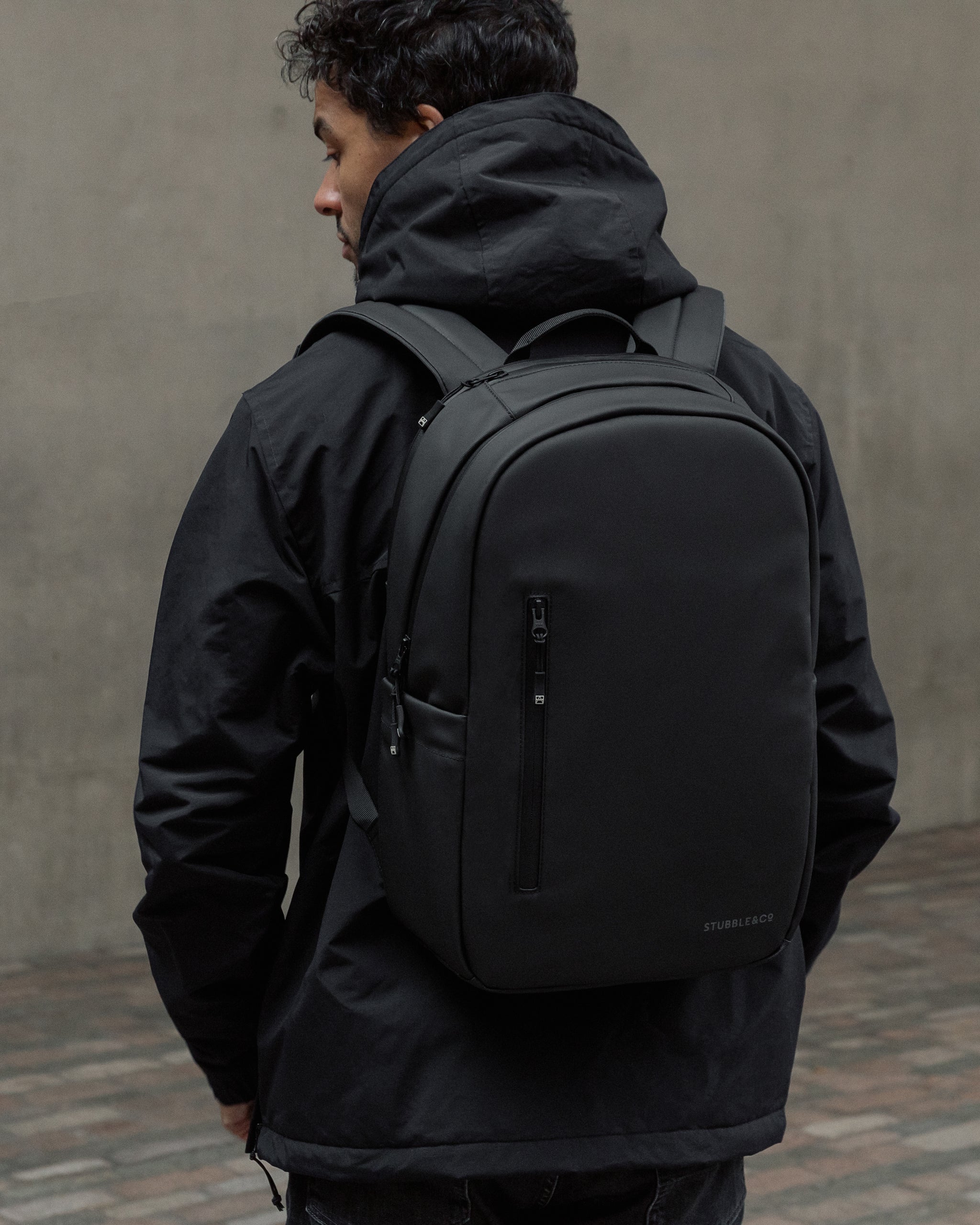 A man facing away wearing an all black everyday backpack on his back