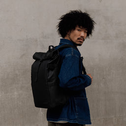 Man in a denim jacket wearing The Roll Top 20L in All Black