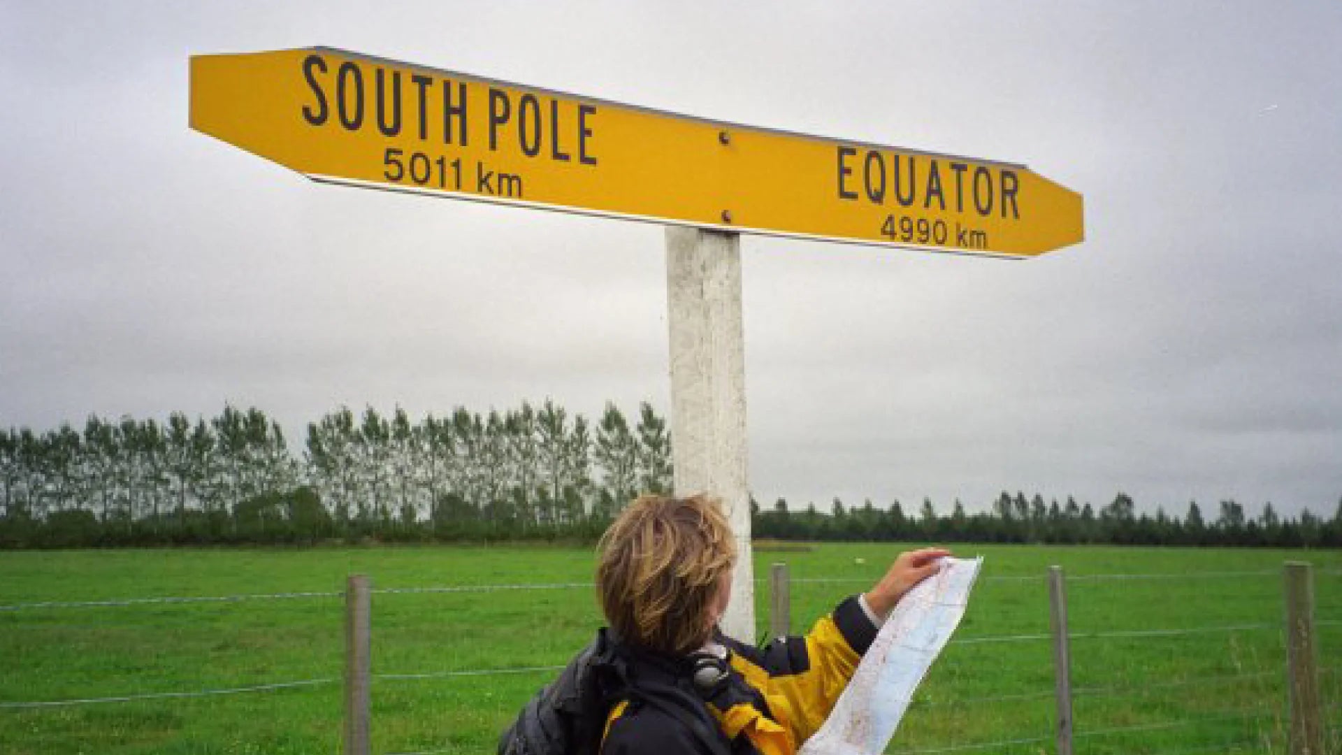 A sign showing a woman reading a map in front of a signpost