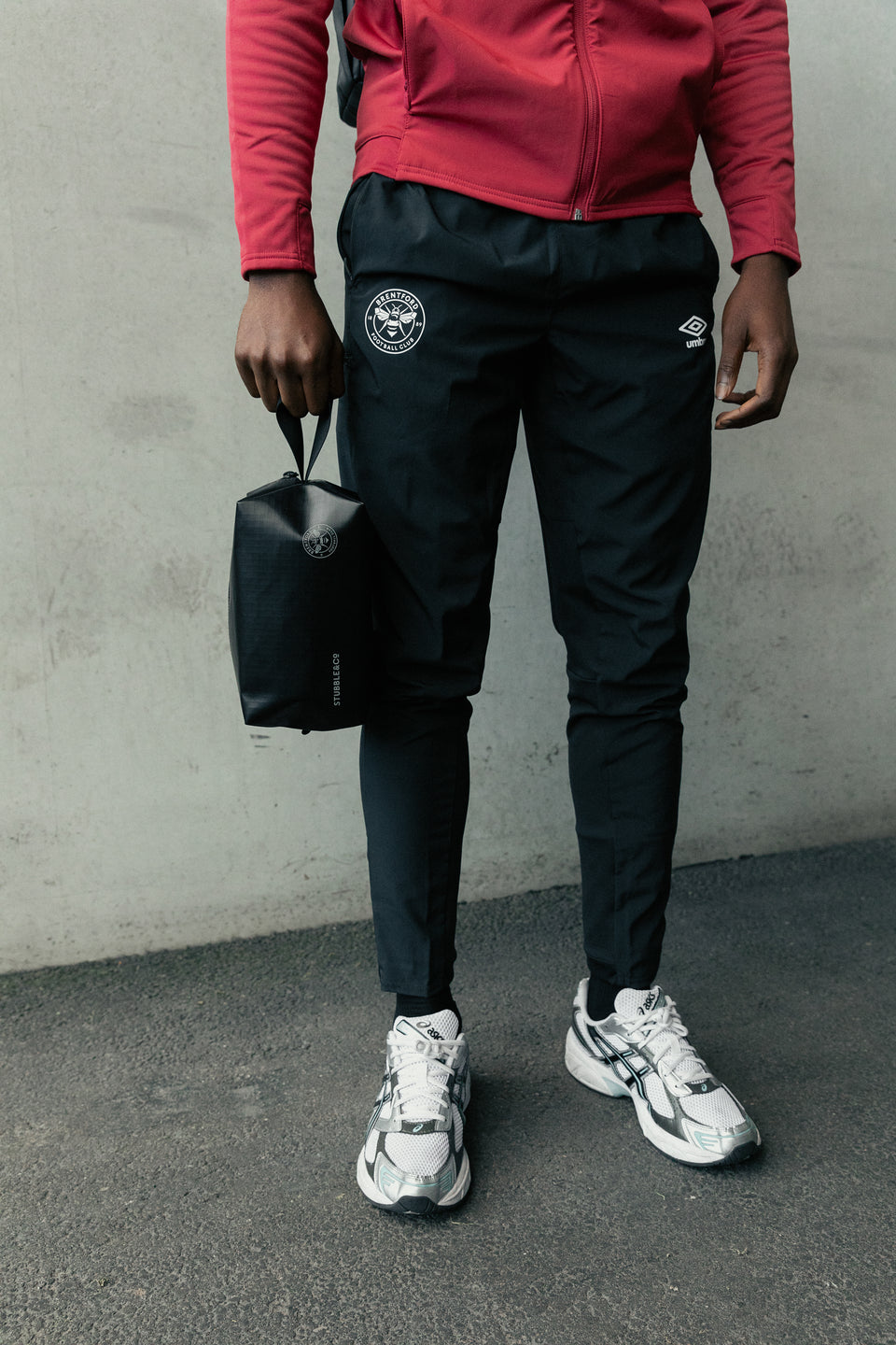 Man standing in front of concrete wall holding a black wash bag by his side