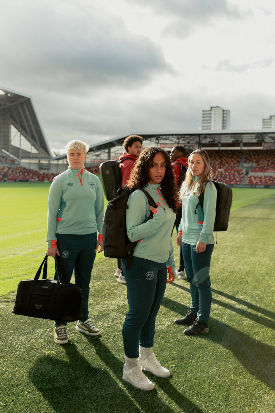 Male and female football players standing on the pitch with a collection of stubble & co backpacks and rucksacks