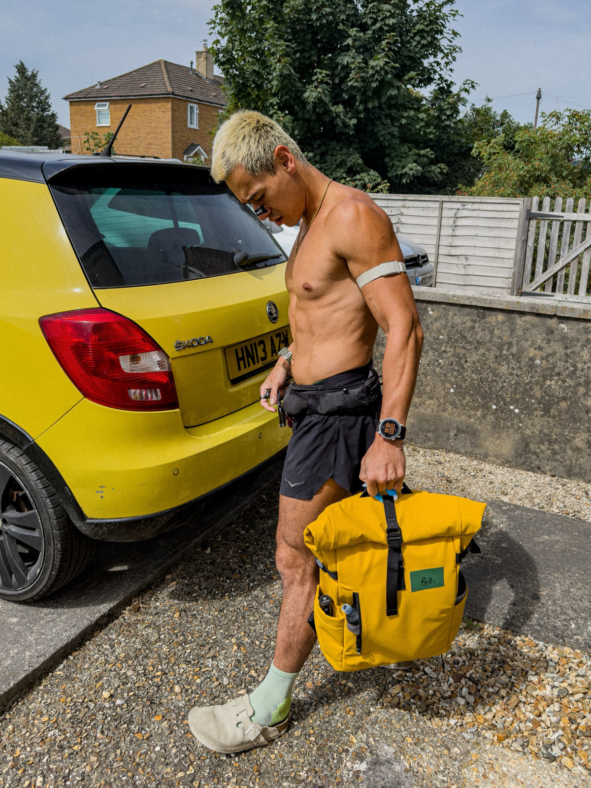Man in running shorts holding The Roll Top in Yellow by its top handle beside a yellow car on a driveway