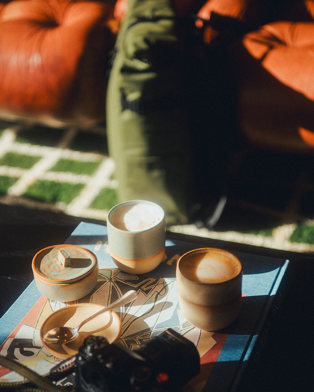 Three coffee cups on a table with a patterned rug and Roll Top in the background