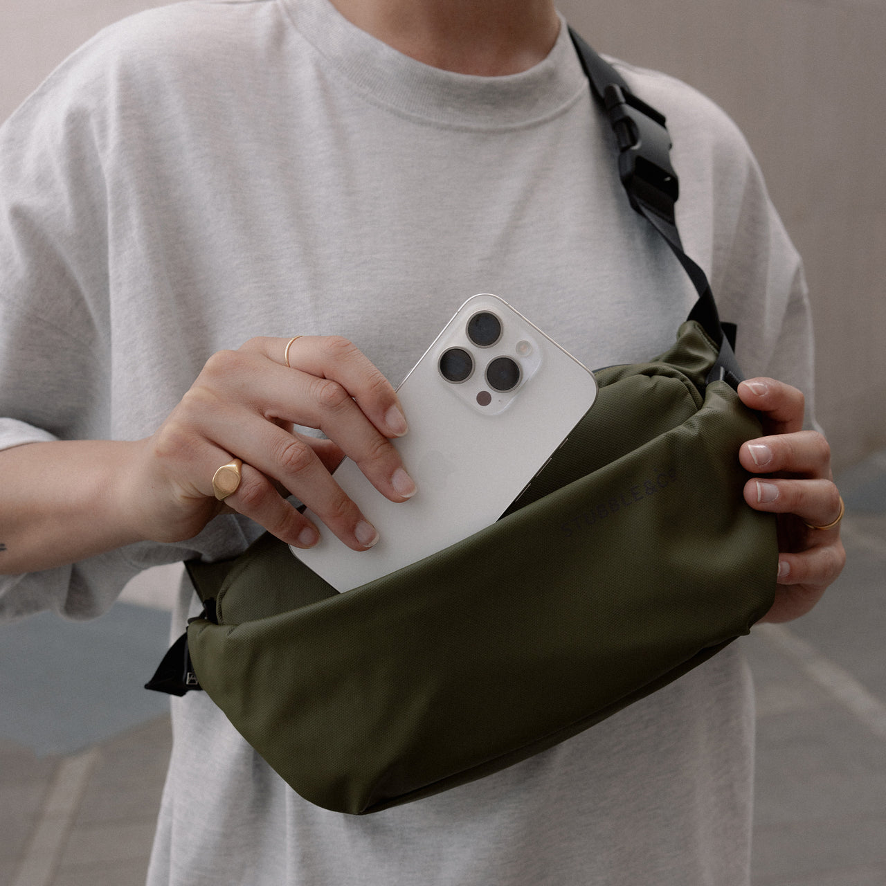 a woman wearing an Urban Green crossbody on her front and putting her phone into the pocket