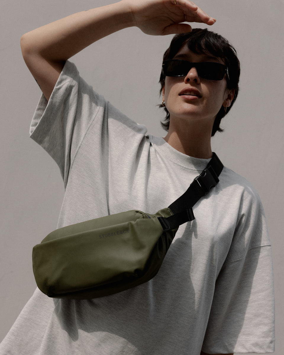 A woman standing in the sunshine wearing an urban green crossbody on her front