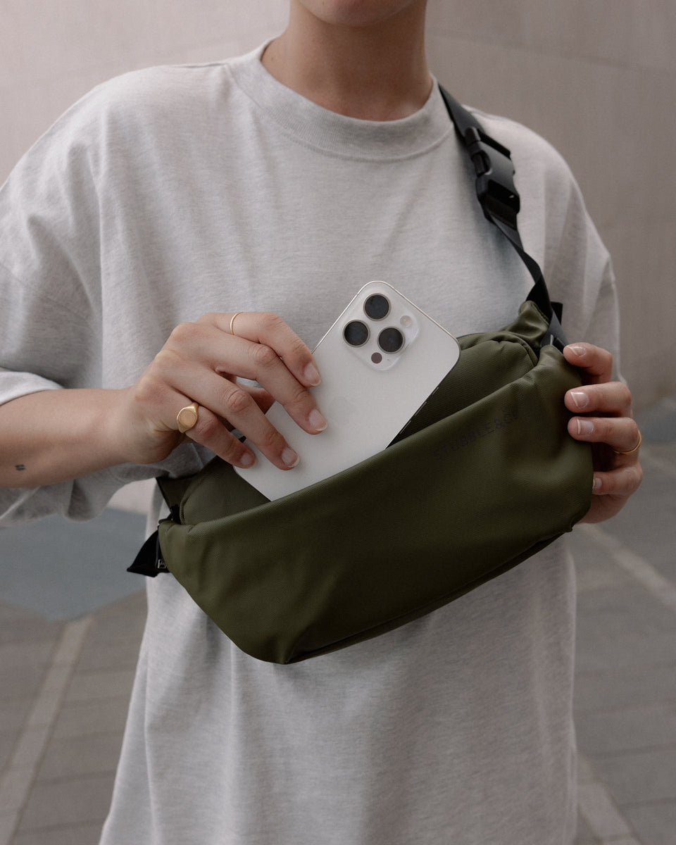 a woman placing a phone in the front pocket of an urban green crossbody