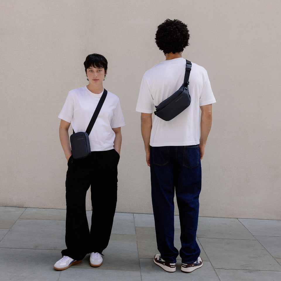 A woman wearing a shoulder bag and a man facing away wearing a Midnight Blue Crossbody across his body