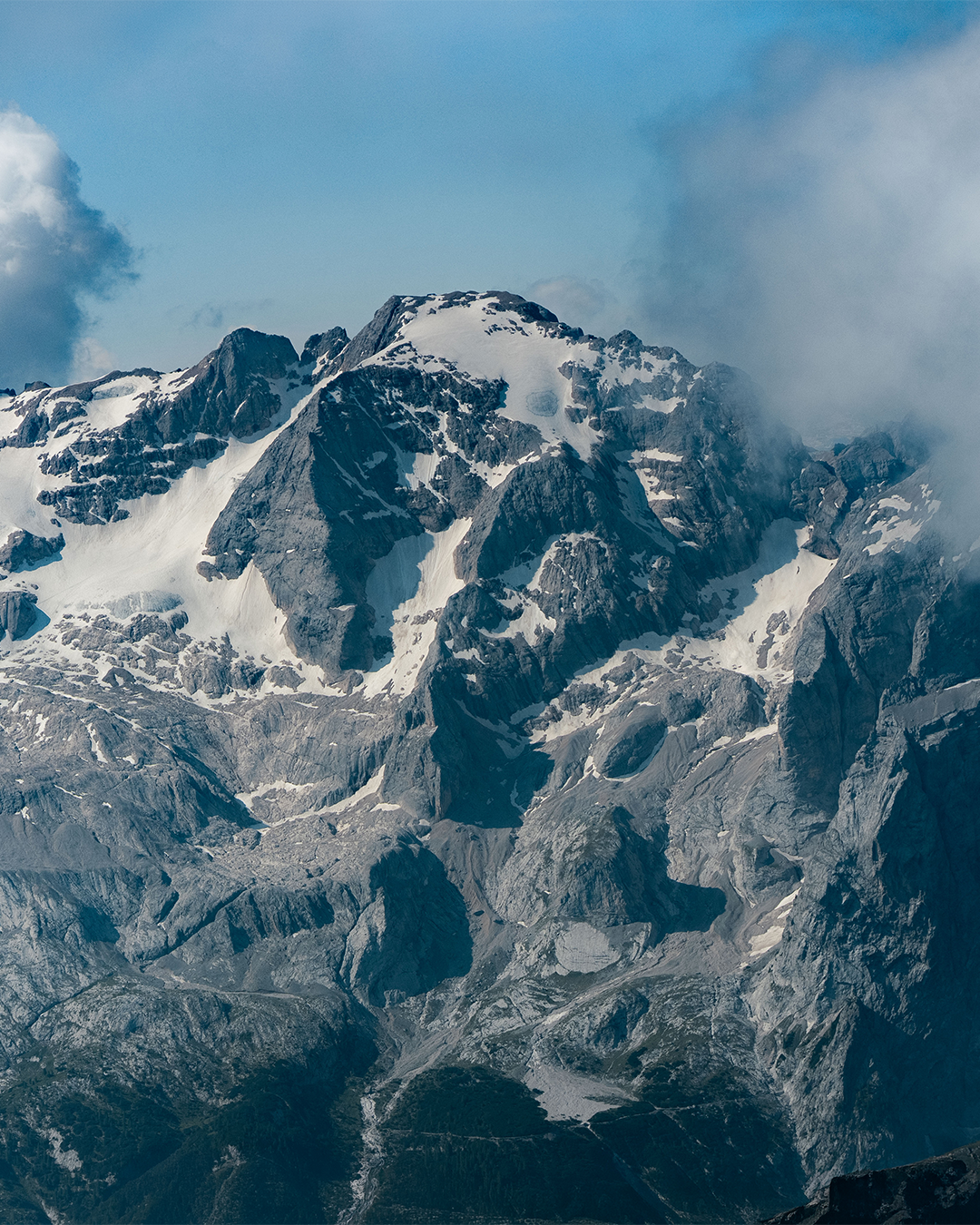 Snow-covered rocky mountain peaks under a blue sky with clouds drifting around the summit.