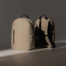 A studio shot of two Everyday Backpack 15L in Sand side by side in a ray of light