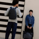  A man wearing an Everyday Backpack 15L in Midnight Blue on his back standing next to a woman holding a Laptop Tote Bag