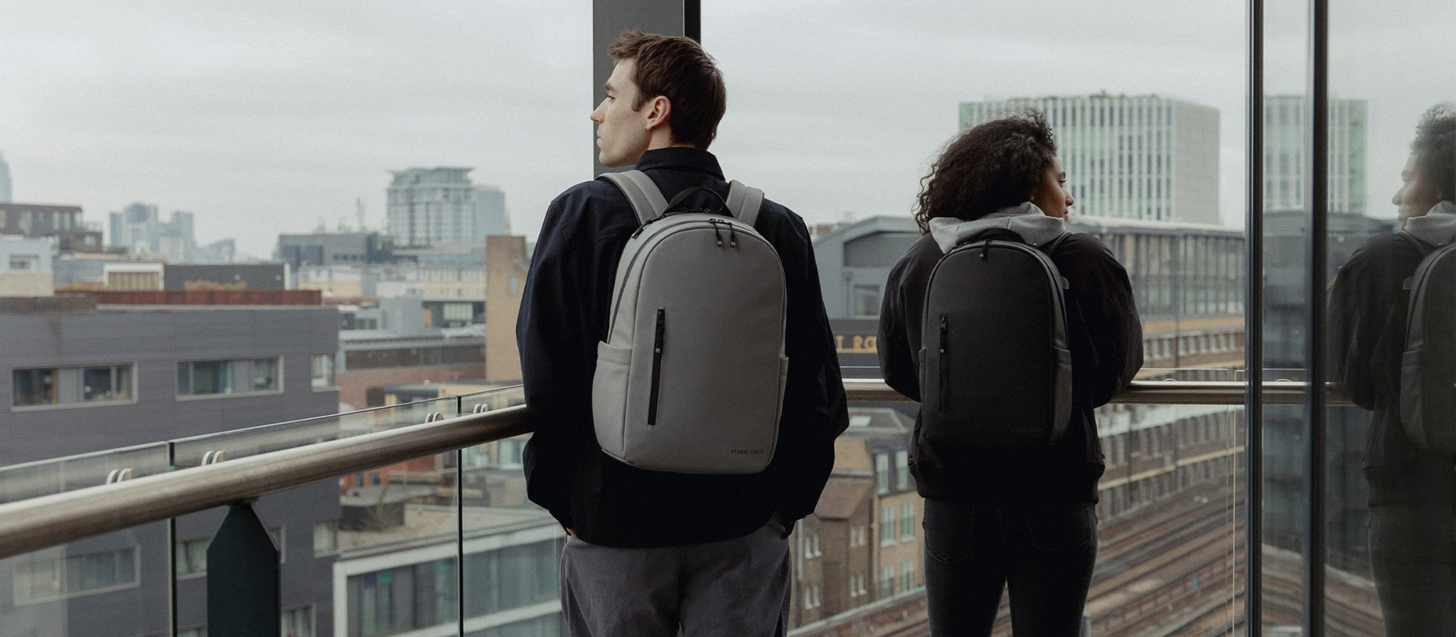 A man and woman wearing everyday backpack 15l on their backs on a balcony above London