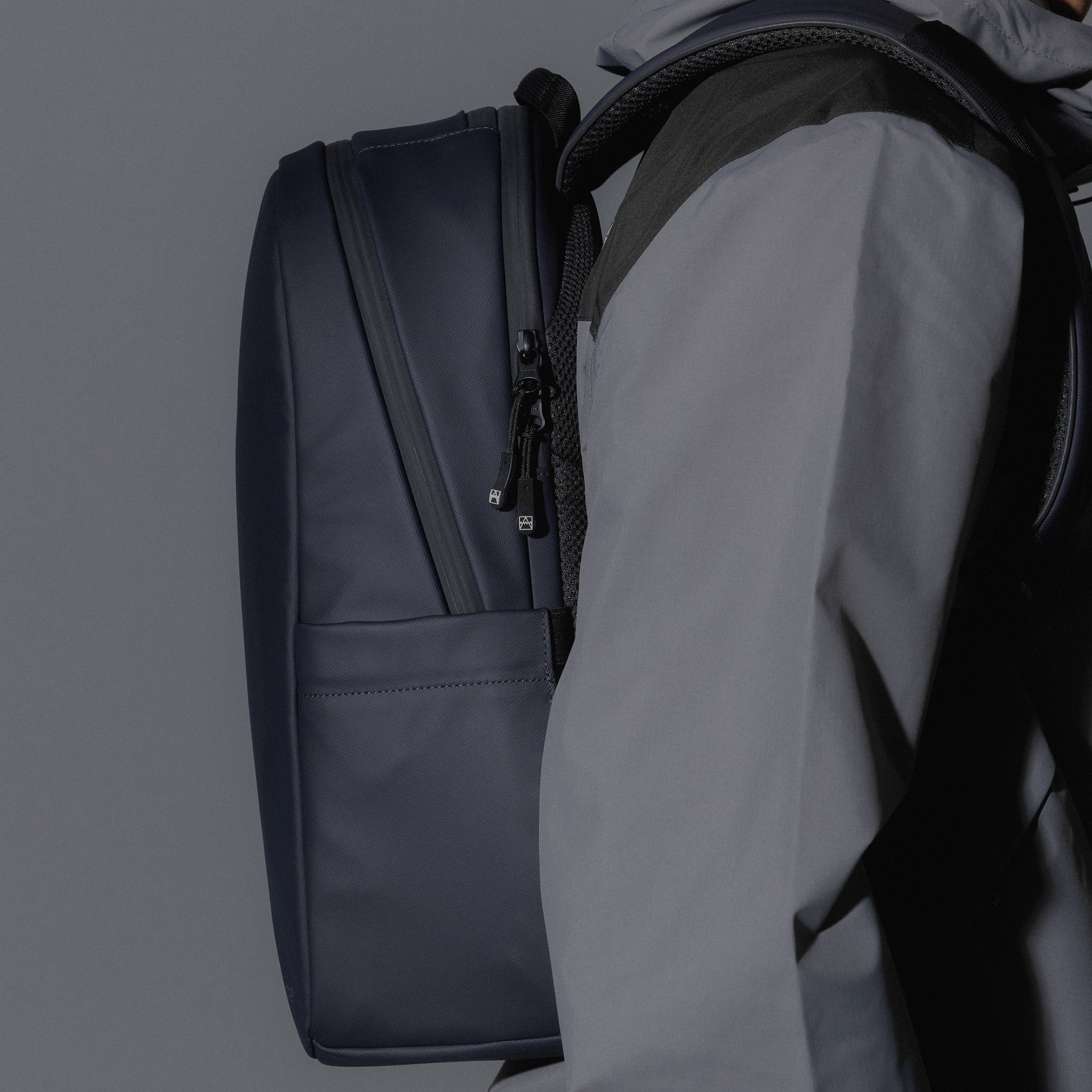 A studio shot of an Everyday Backpack 15L in Midnight Blue showing a close up of the bag on a mans back