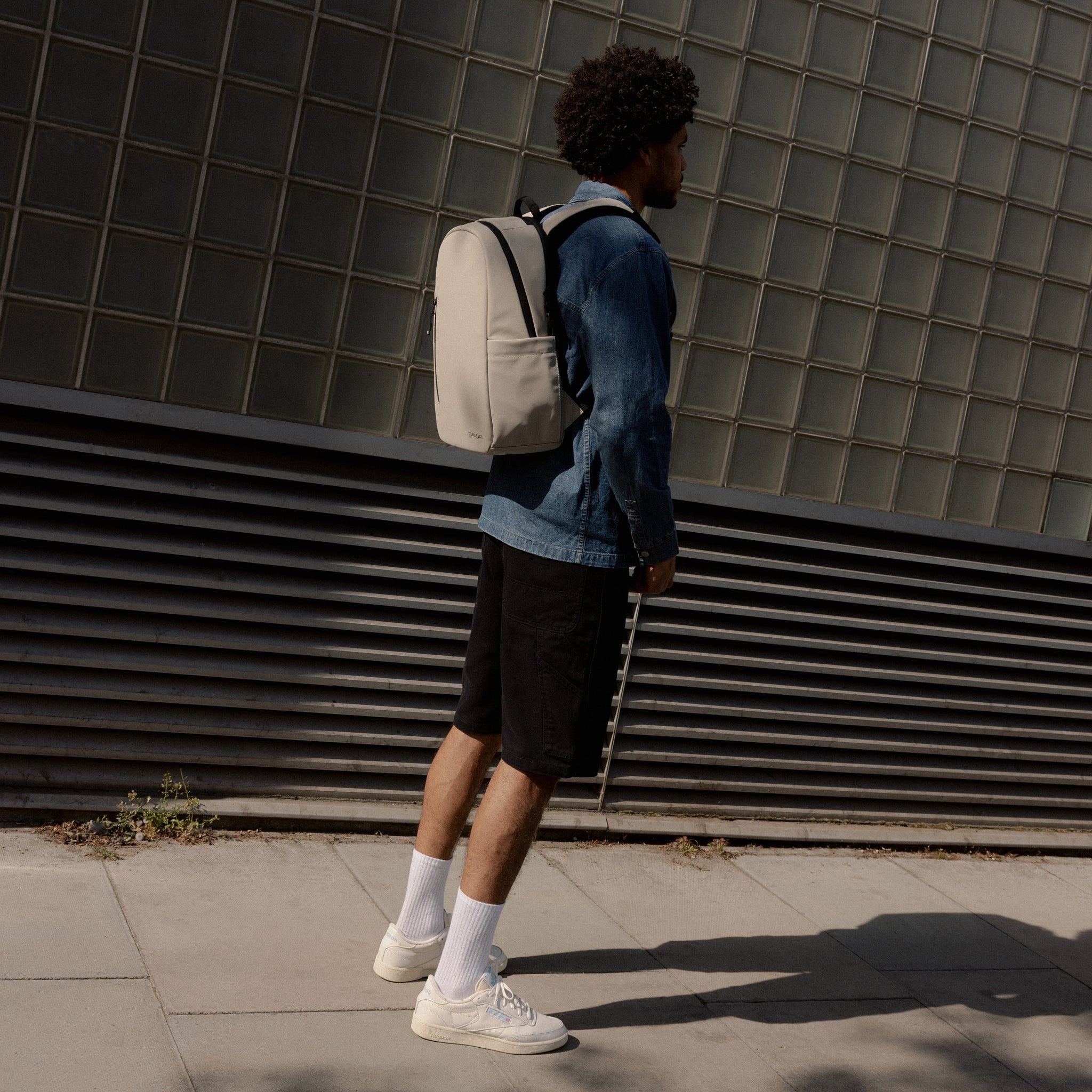A man standing in the street wearing an Everyday Backpack 20L in Sand on his back